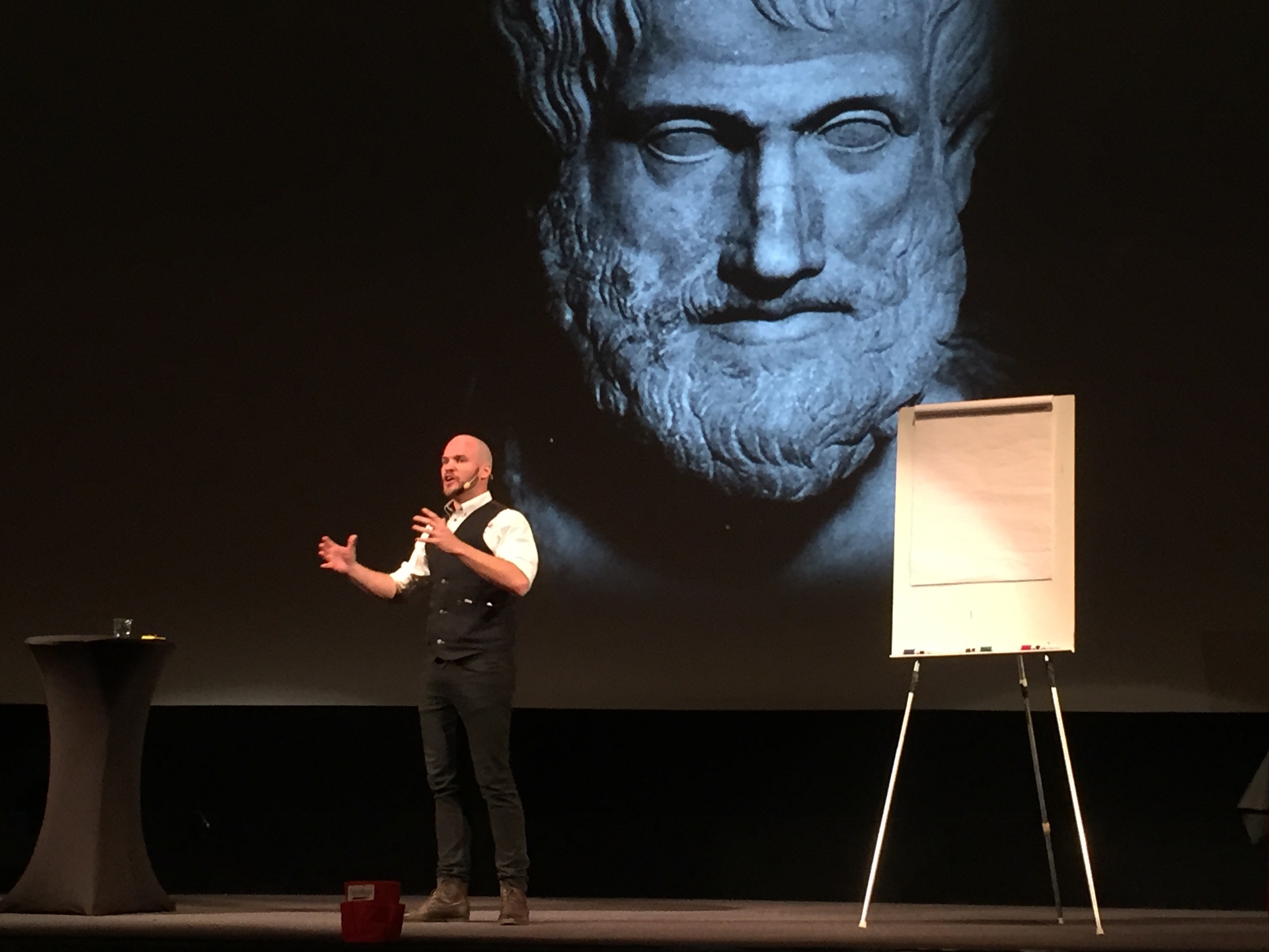 Alex on stage, Aristotle bust projected behind him